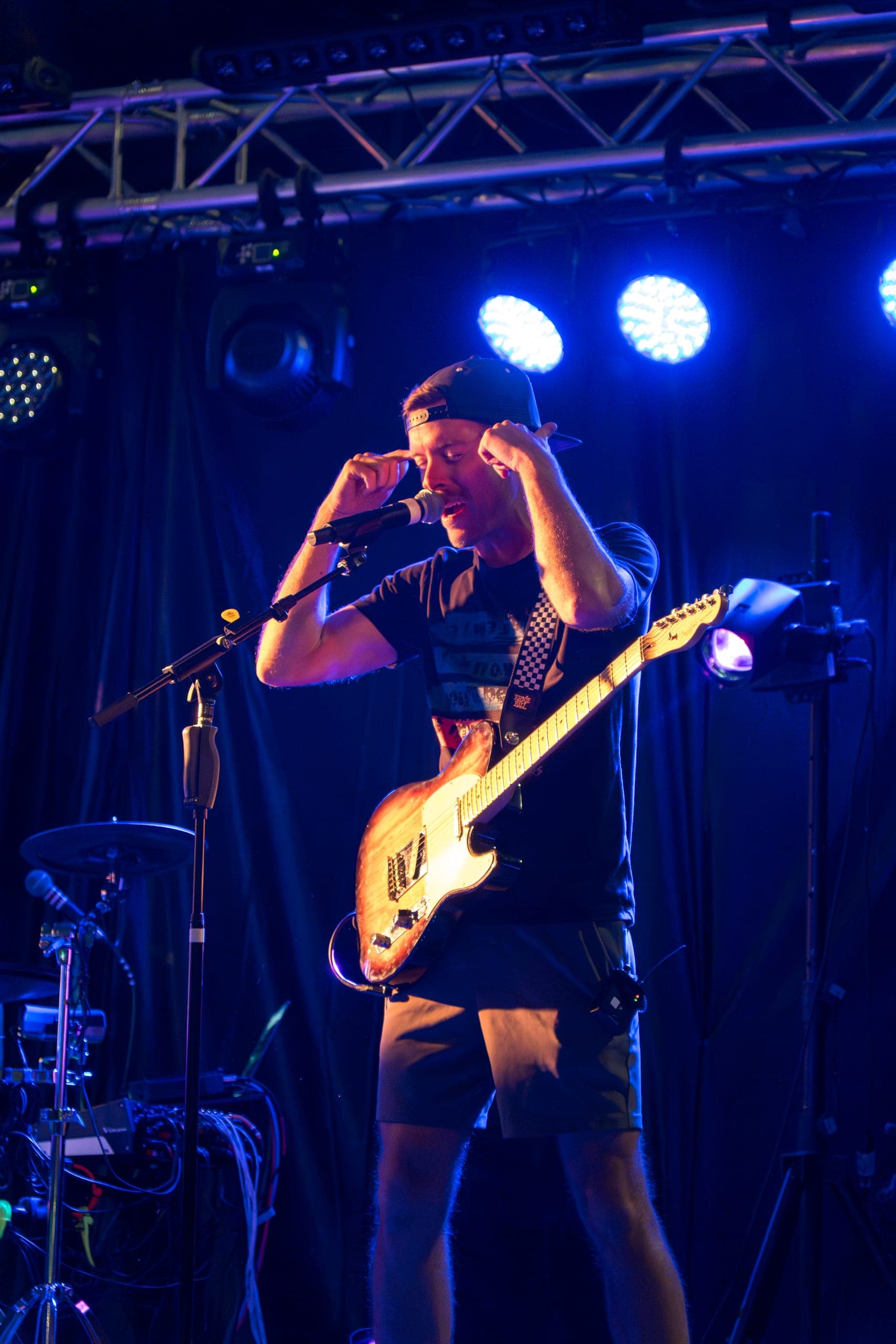 Guitarist in a backwards cap singing at the mic under blue lights