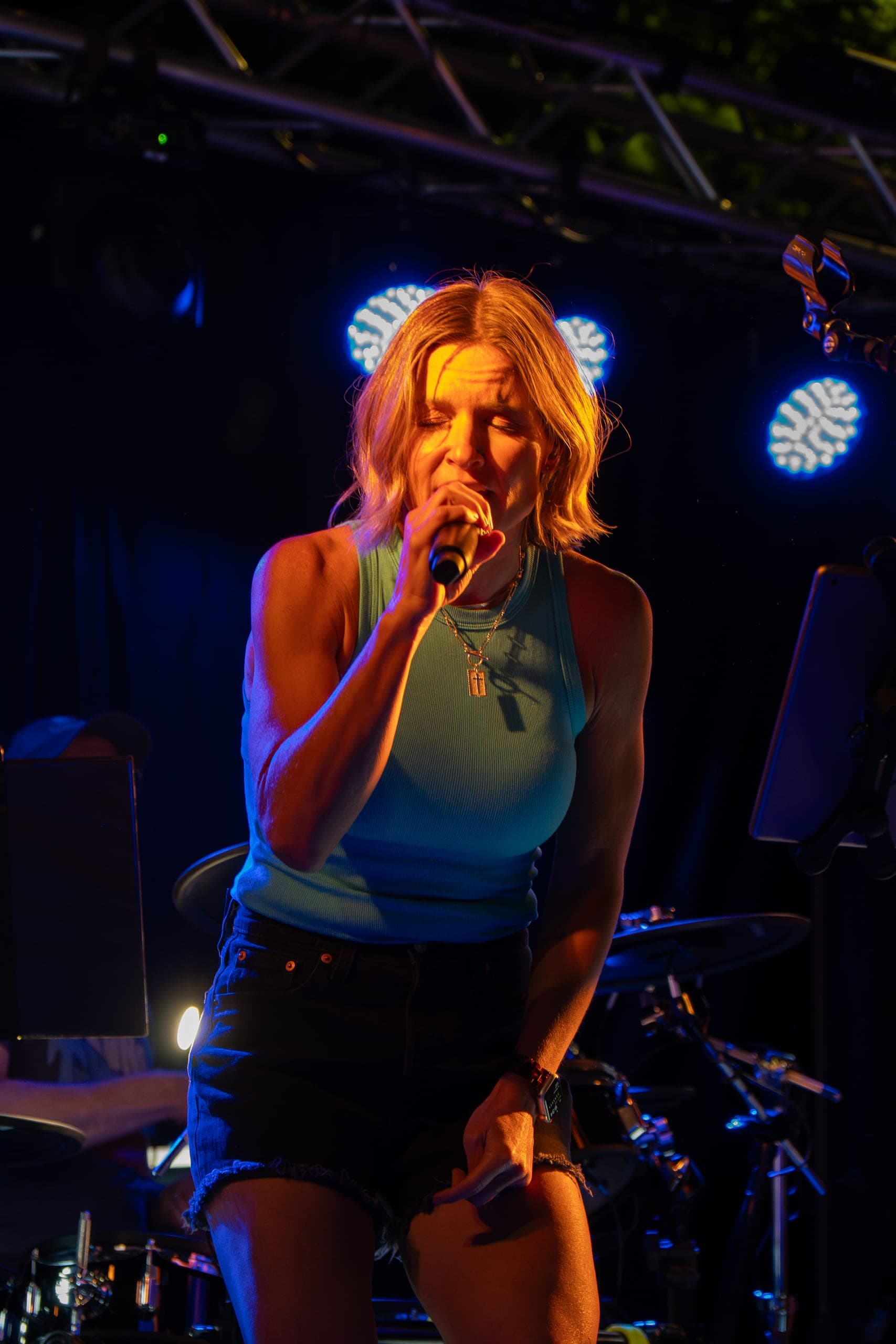 Lead vocalist singing into the mic under warm and blue stage light